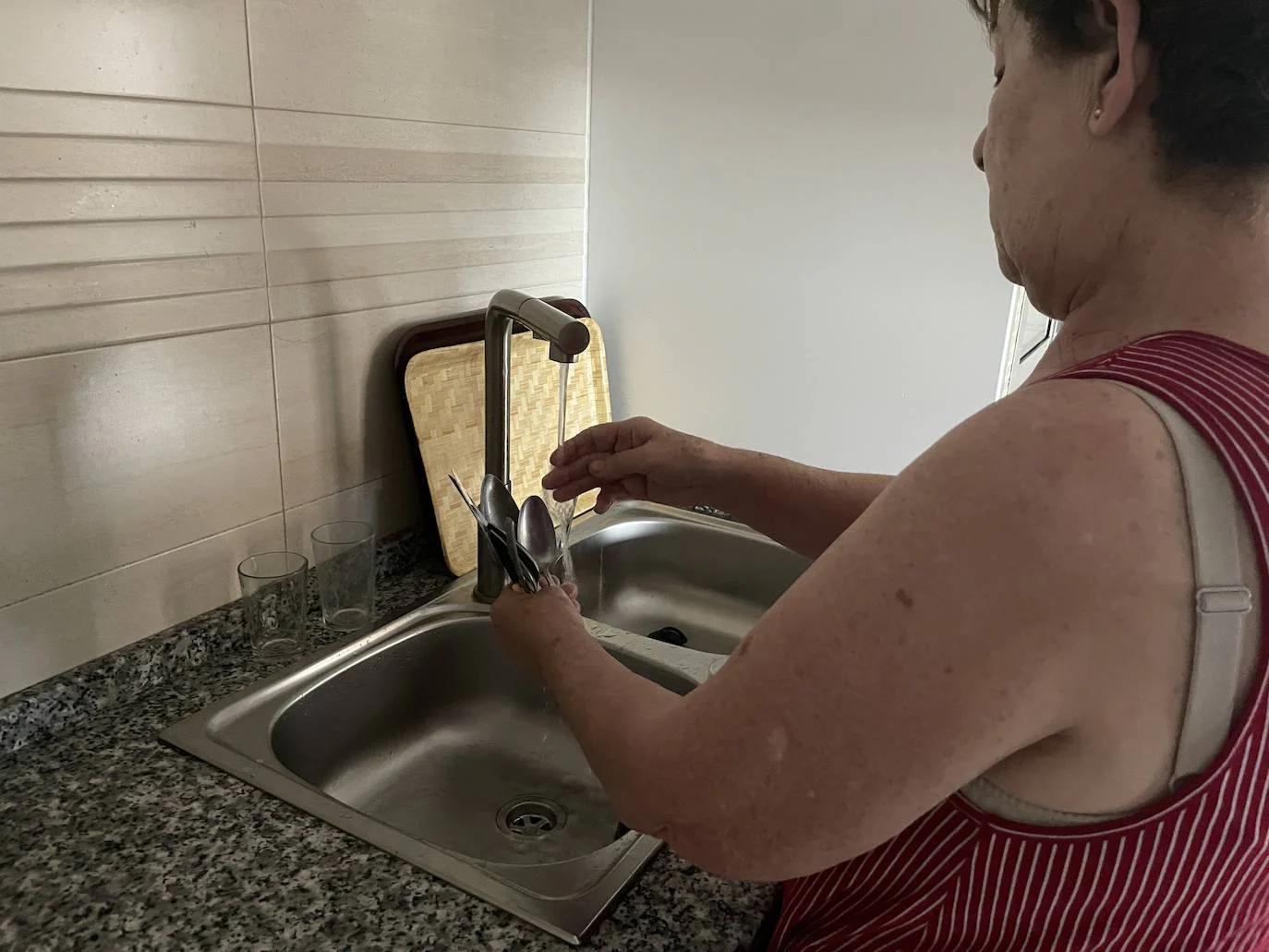 Una vecina de Tentudía lava sus utensilios de cocina bajo el grifo 