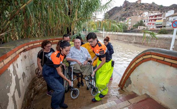 Voluntarios de protección civil trasladan a un hombre en silla de ruedas tras las intensas lluvias en Blanca (Murcia).