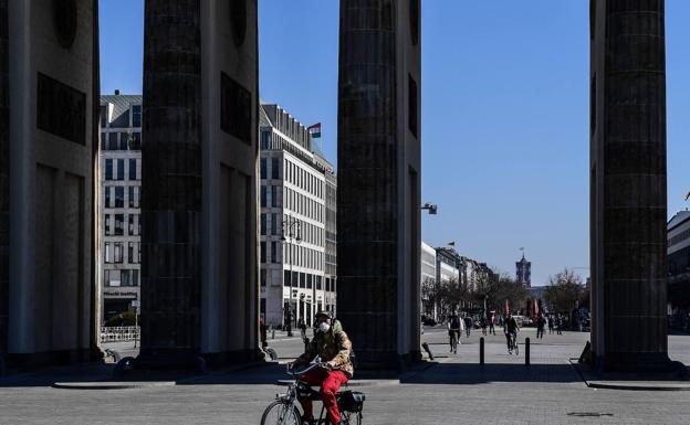 Un ciclista con mascarilla pasa por la Puerta de Brandenburgo en Berín/EFE